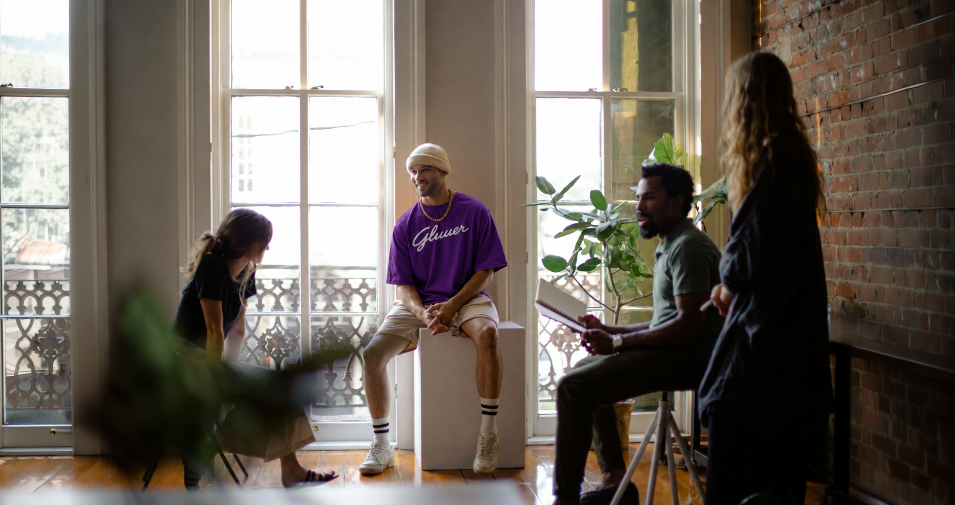 The Gluuer team talking together in a sunlit studio, with founder Berto Macario wearing a purple Gluuer shirt